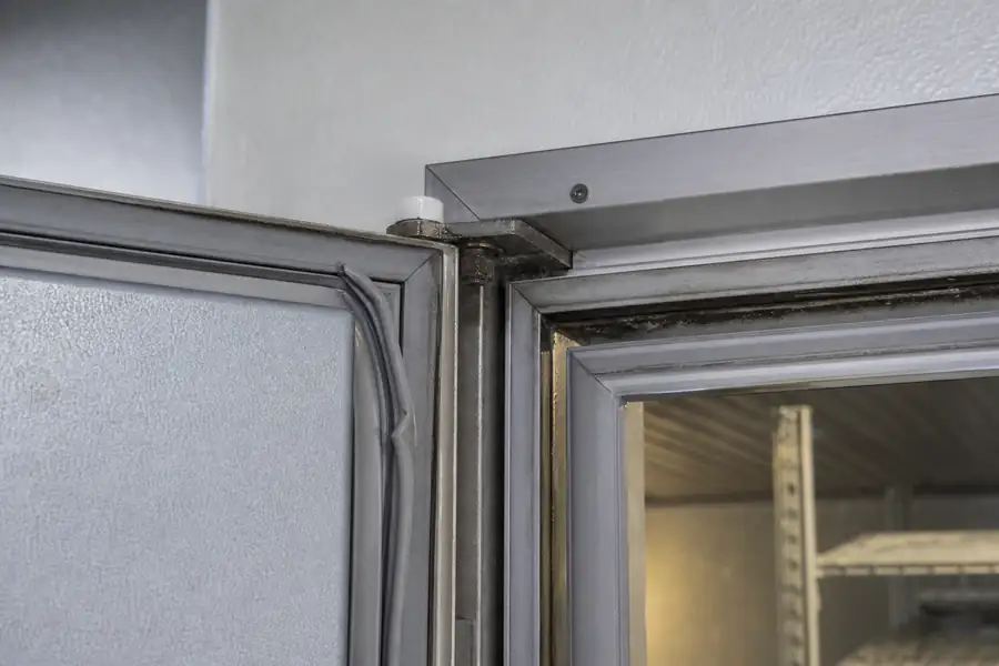 High-detail documentary for “Replacing a Commercial Gasket Yourself: When It Works and When It Costs More.” Show unseated corner. Focus on the gasket profile, mitre, magnetic strip, retaining channel, hinge, latch, measurement point or visible failure pattern that supports the article’s explanation. Relevant equipment: Reach-ins; prep tables; walk-in swing doors. Relevant manufacturers when naturally visible: Contextual. Realistic commercial-kitchen surfaces, accurate proportions, no added labels or text, horizontal composition.